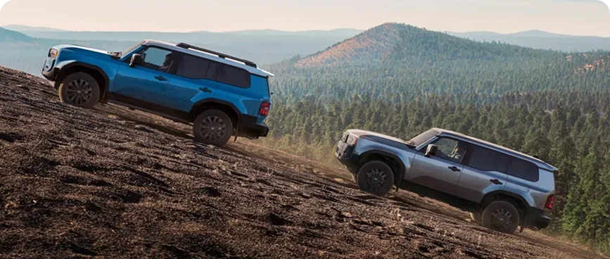Two blue Land Cruisers descending a steep dirt slope