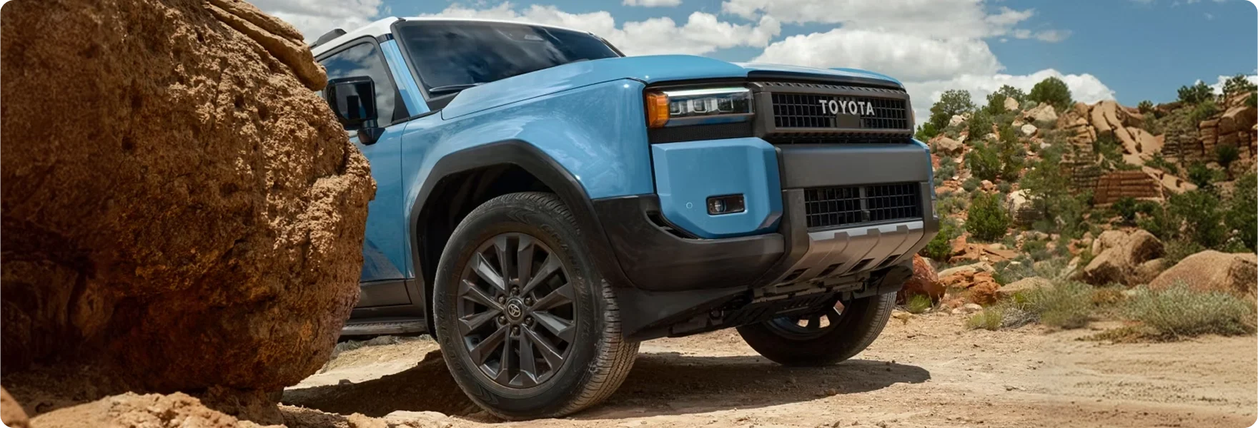 Blue 2027 Toyota Land Cruiser climbing over large red rocks in the desert