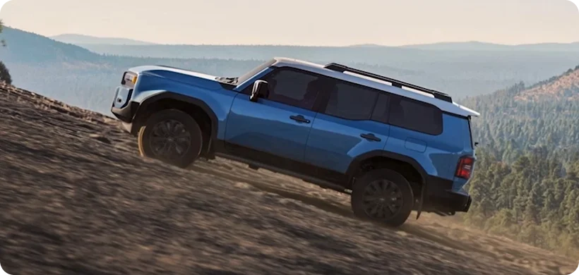 Blue 2027 Toyota Land Cruiser climbing a dirt ridge with rolling hills in the distance