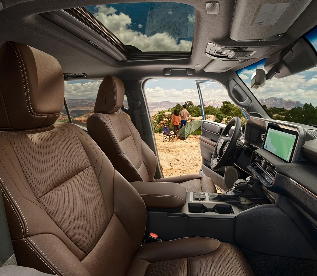 Land Cruiser front cabin with leather seats, dashboard touchscreen and an open door framing a desert campsite
