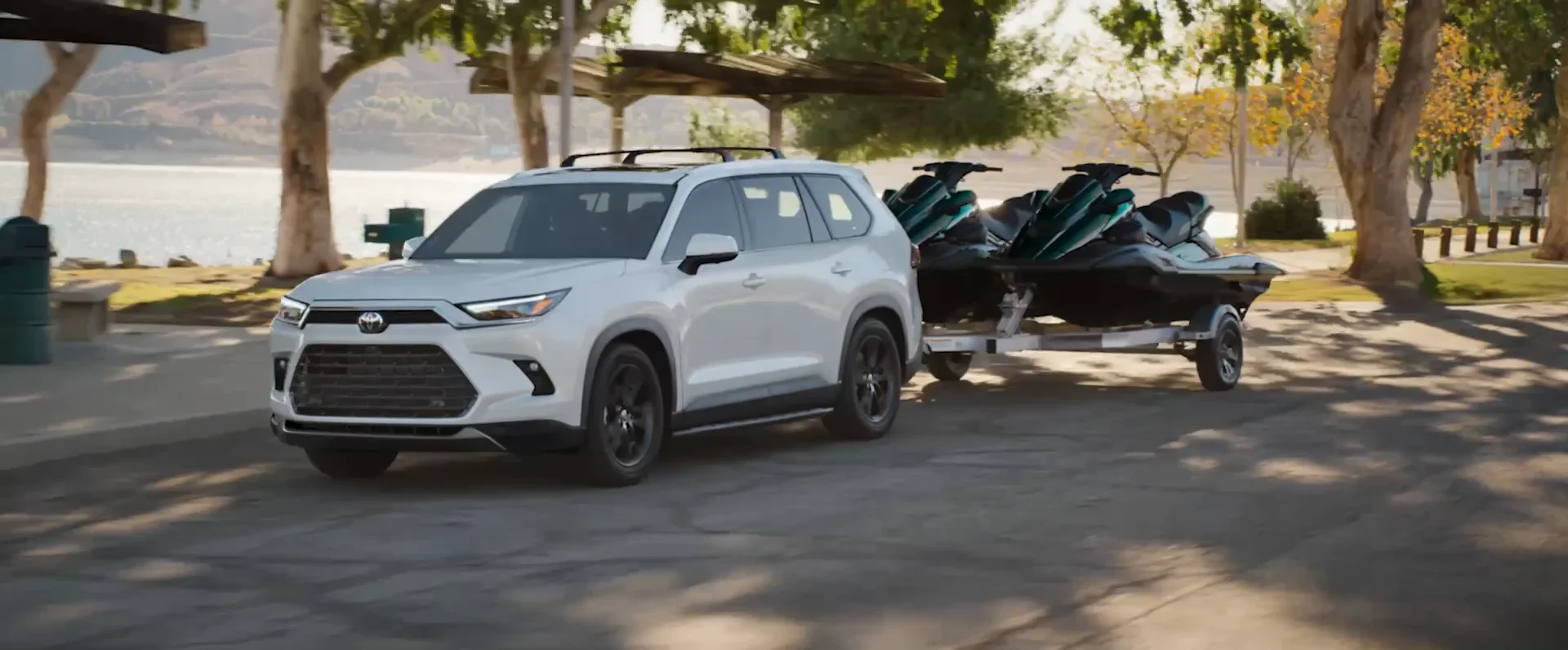 2026 Toyota Grand Highlander towing jet-skis on a lakeside road — Dalton Toyota National City