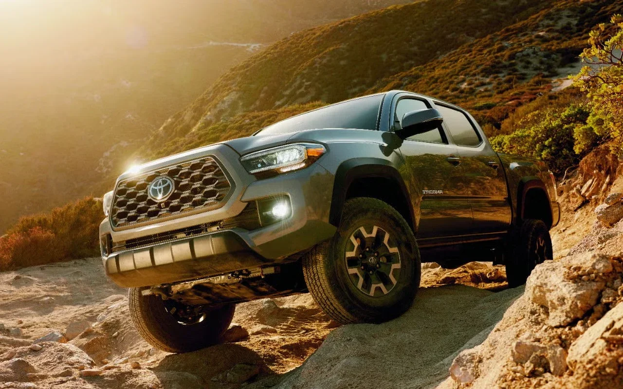 Gray Toyota Tacoma TRD Off-Road climbing rocky terrain at golden hour, front three-quarter view — used trucks at Dalton Toyota National City, CA