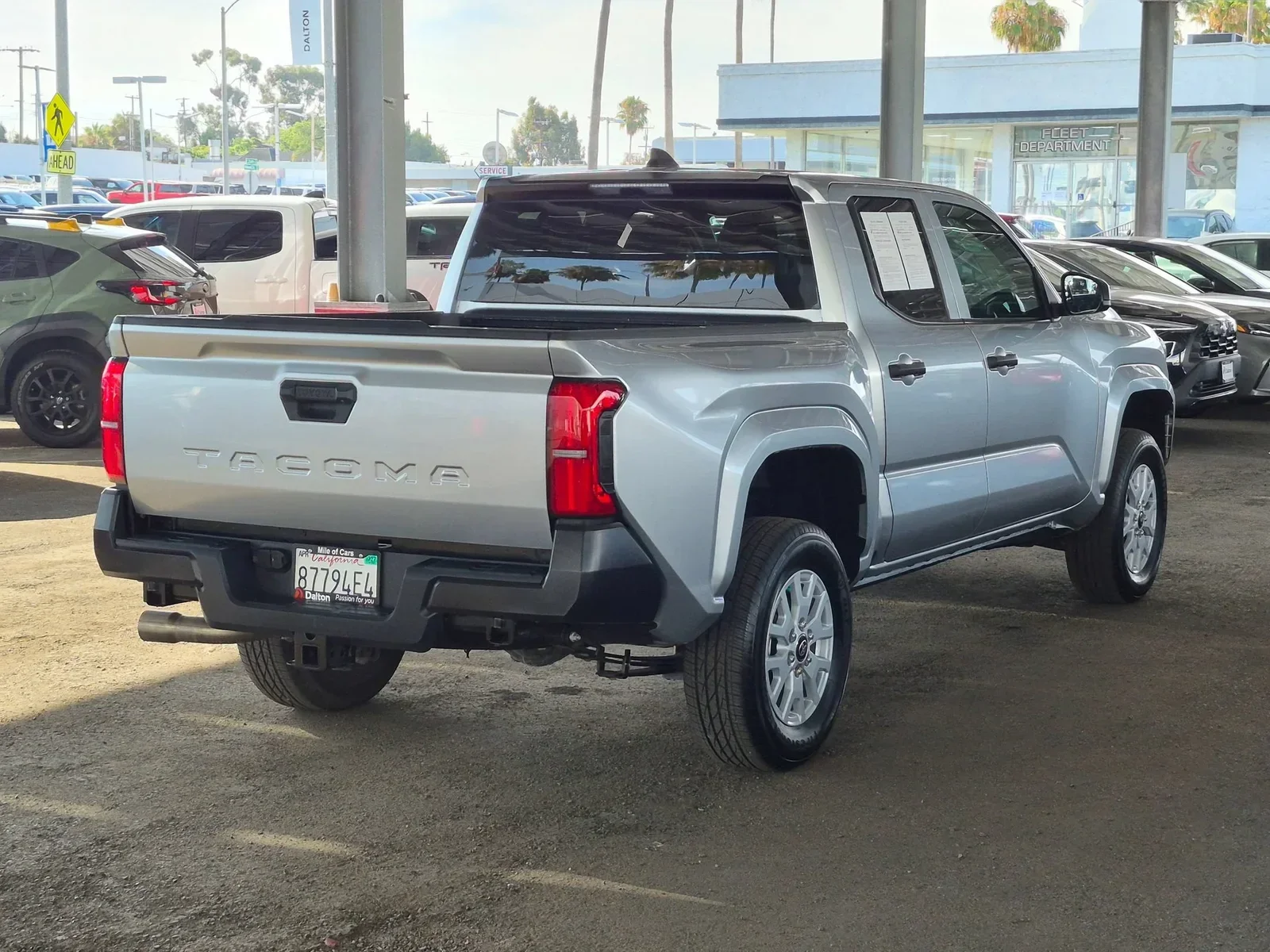 Silver 2025 Toyota Tacoma SR, rear three-quarter view showing bed and TACOMA tailgate, at Dalton Toyota National City