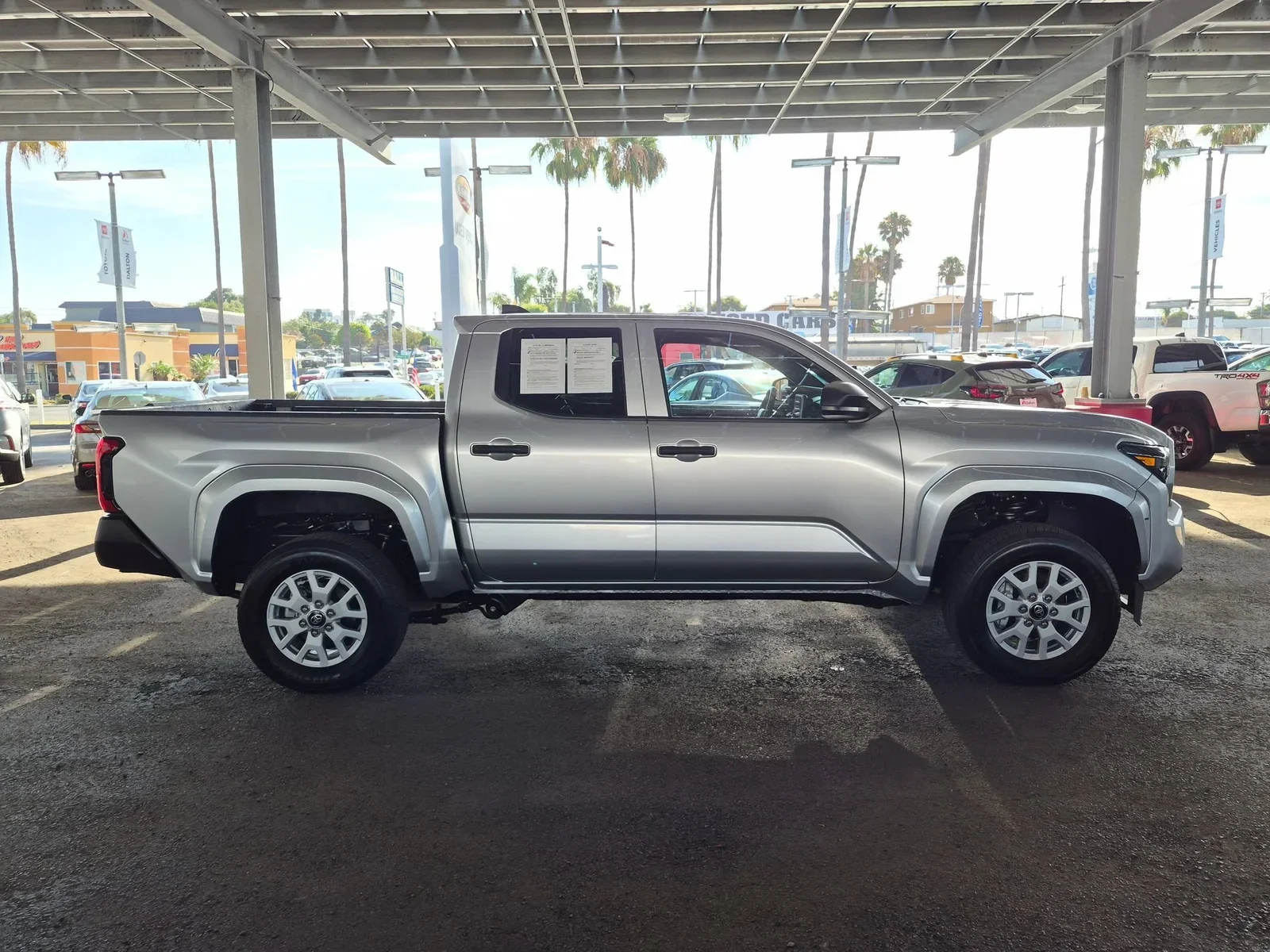 Silver 2025 Toyota Tacoma SR, full side profile, parked under the covered lot at Dalton Toyota on the Mile of Cars
