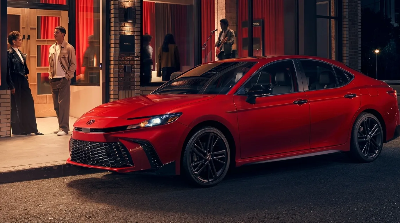 A red Toyota Camry parked on a city street at night outside a lit venue