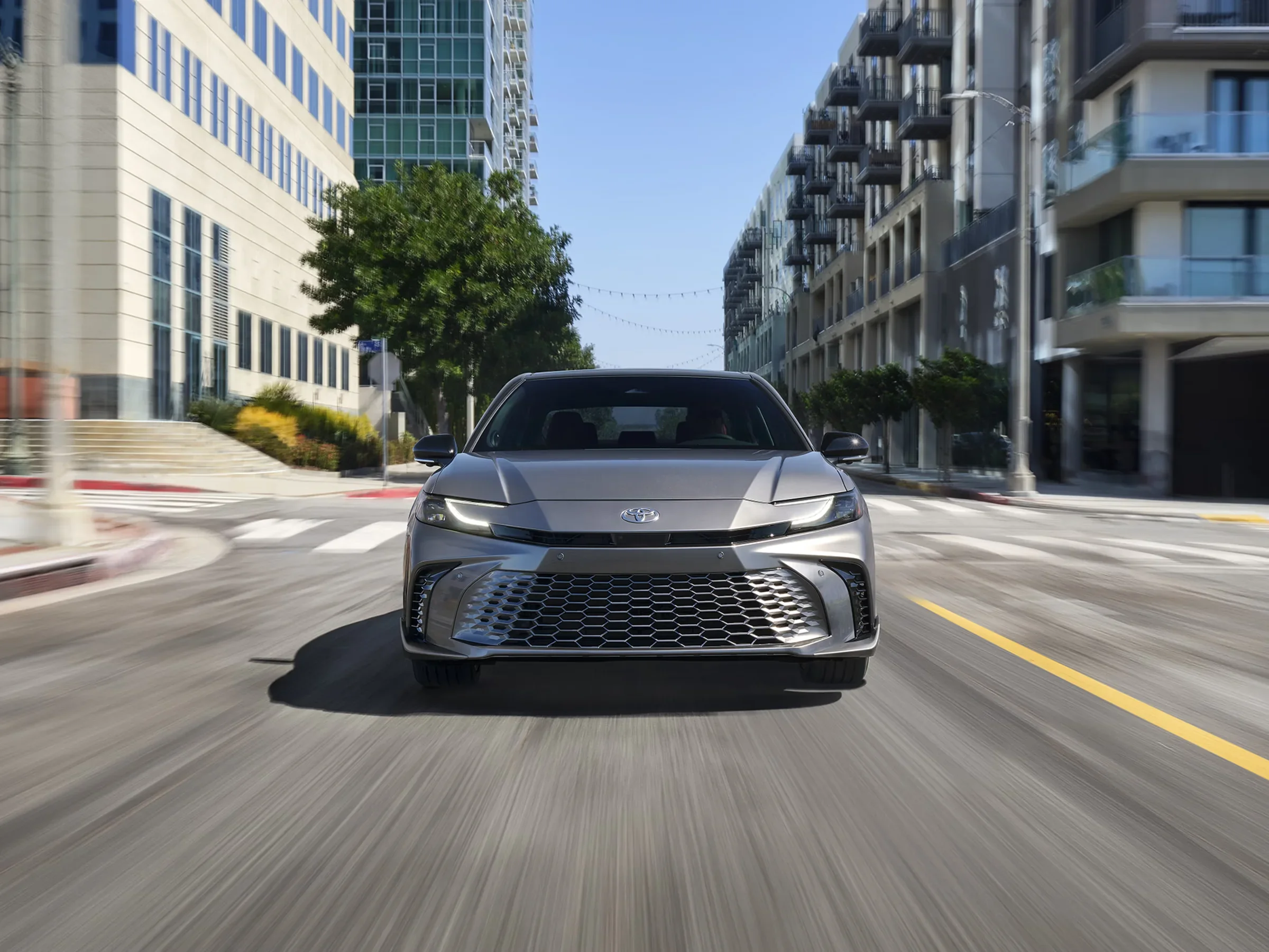 A gray Toyota Camry driving toward the camera on a downtown street