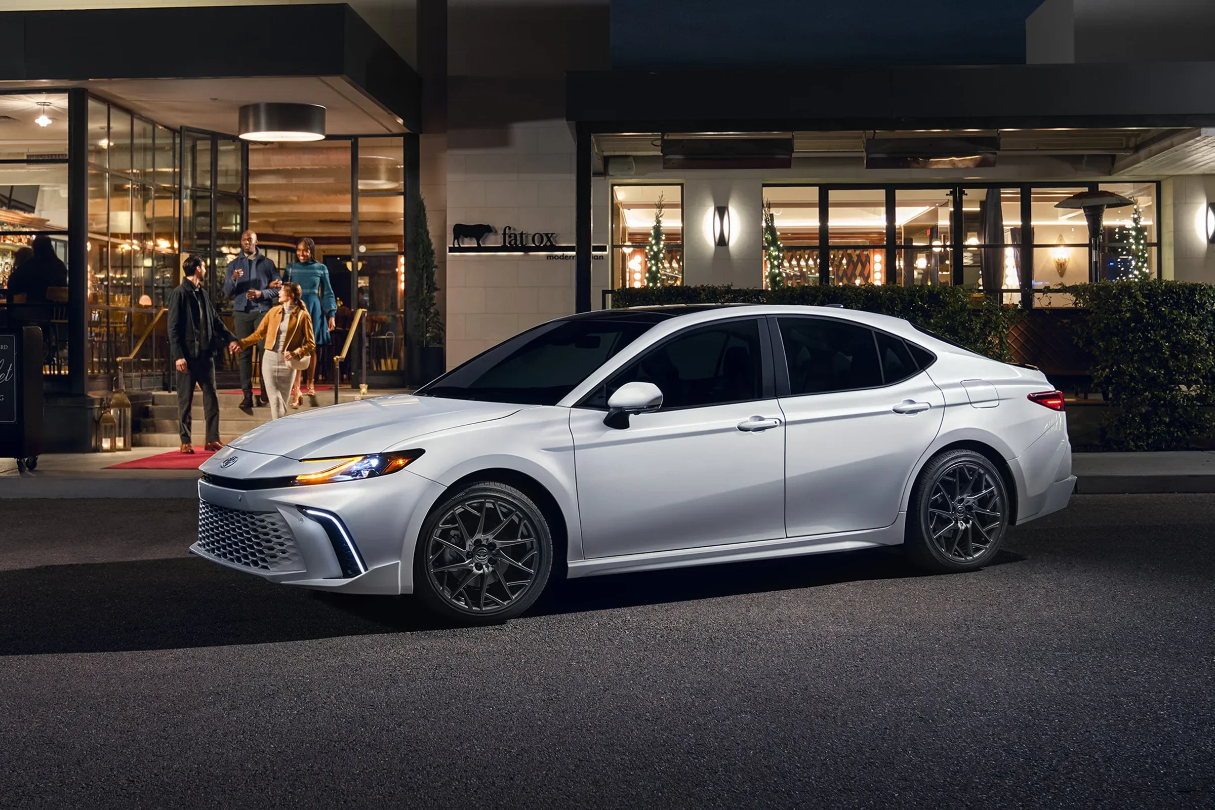 A white Toyota Camry outside lit storefronts at night