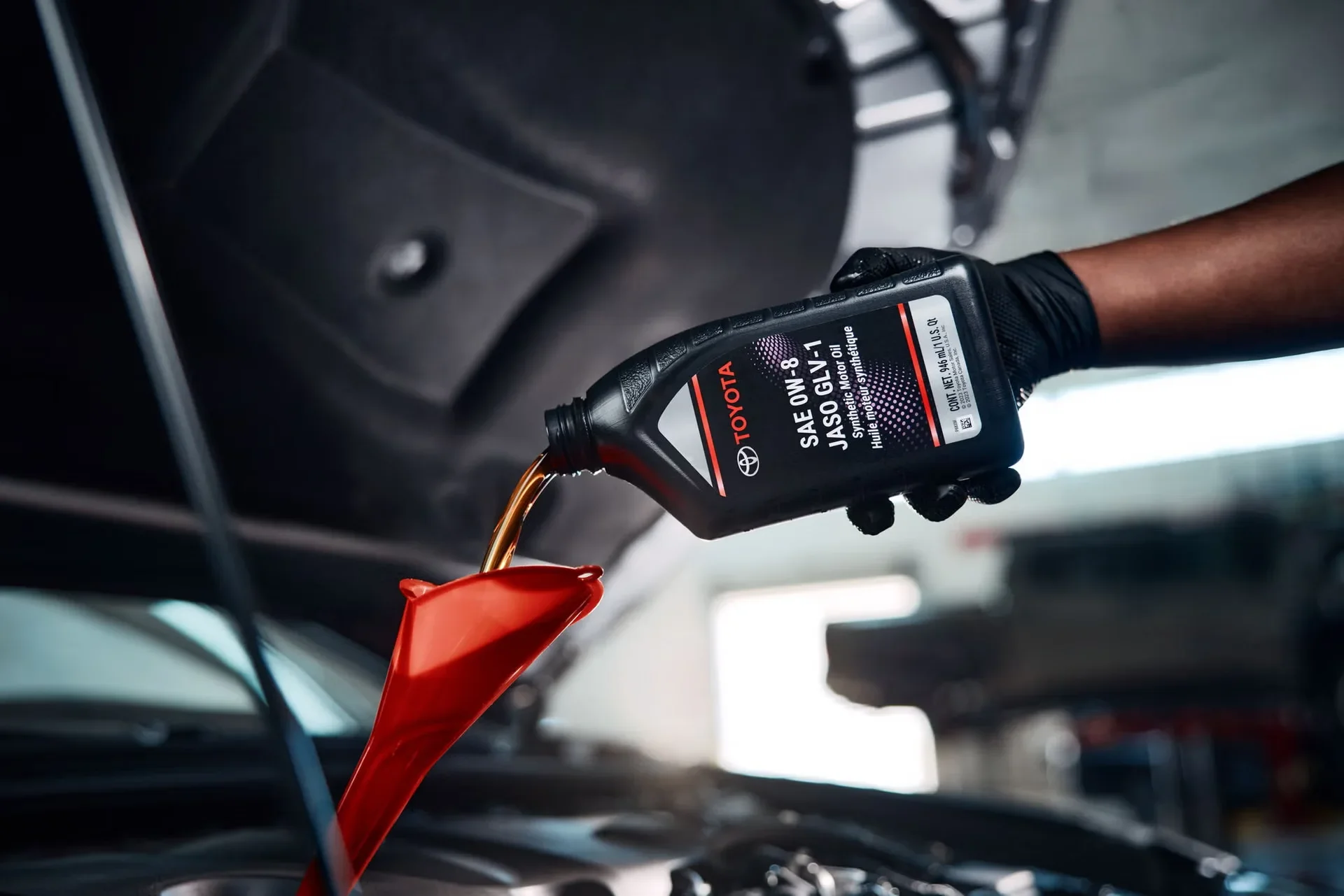 Toyota motor oil poured through a red funnel into the engine