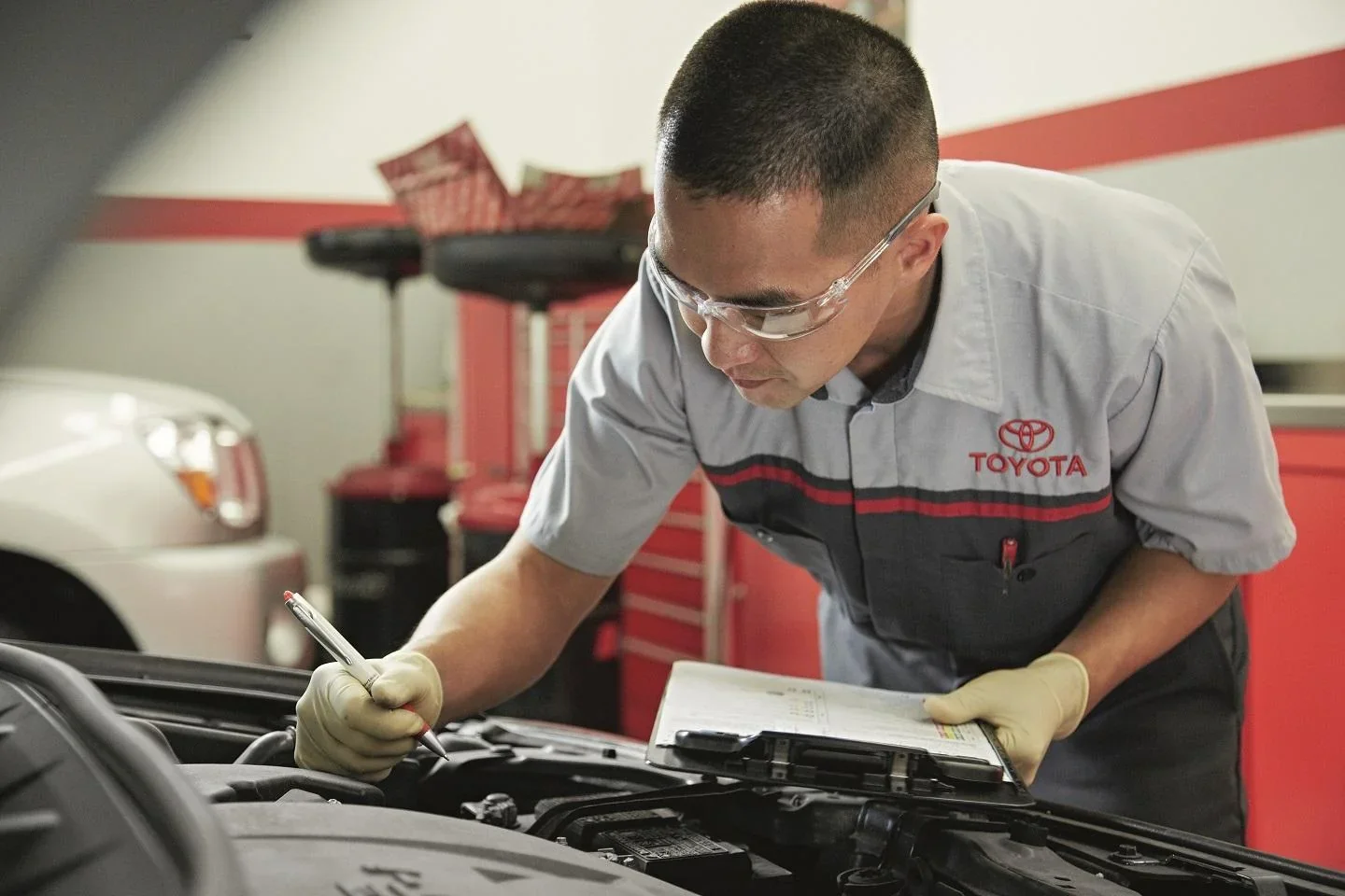 A Toyota technician noting the inspection at the open engine bay