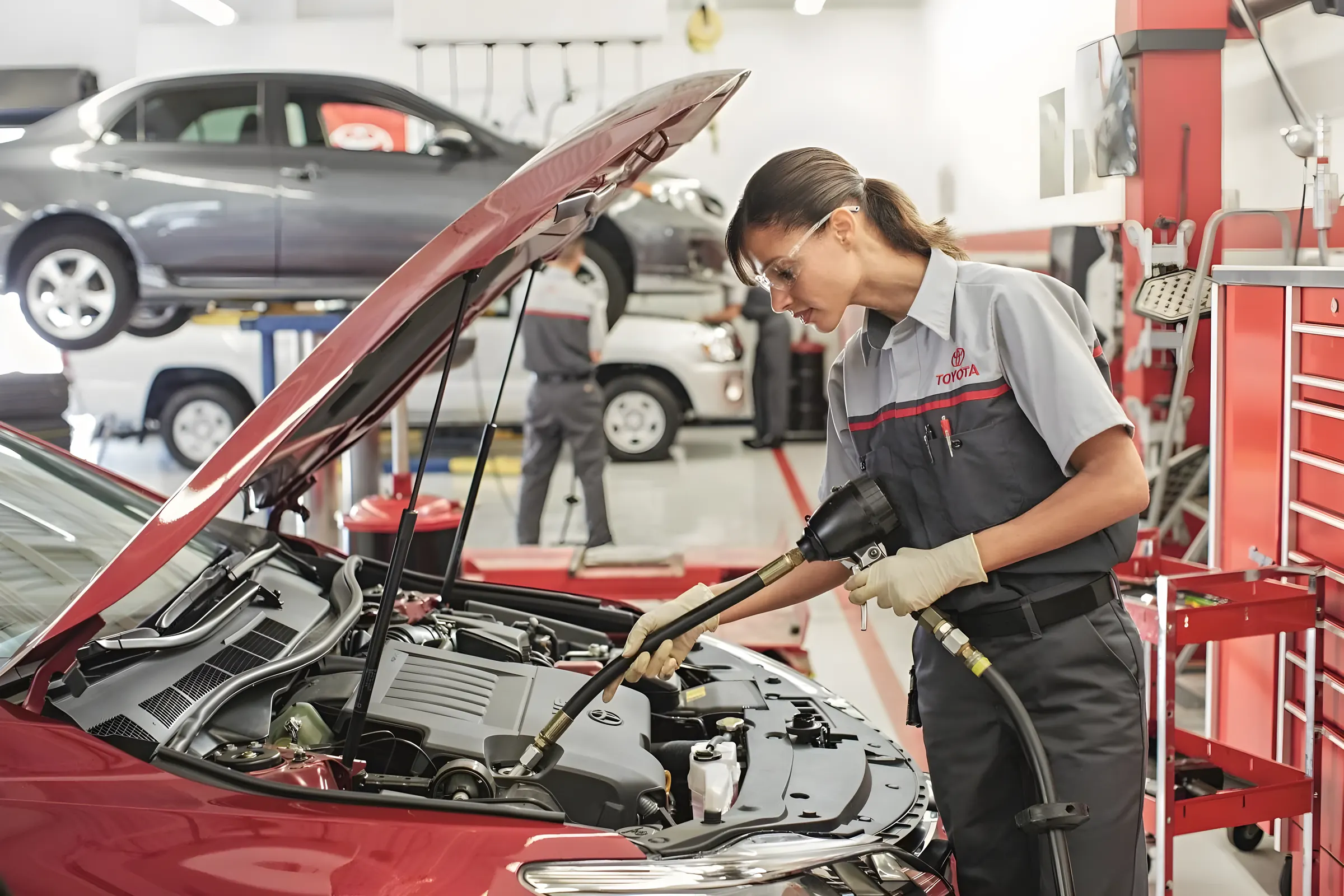 A Toyota technician adding oil at the open hood of a car in our service bay
