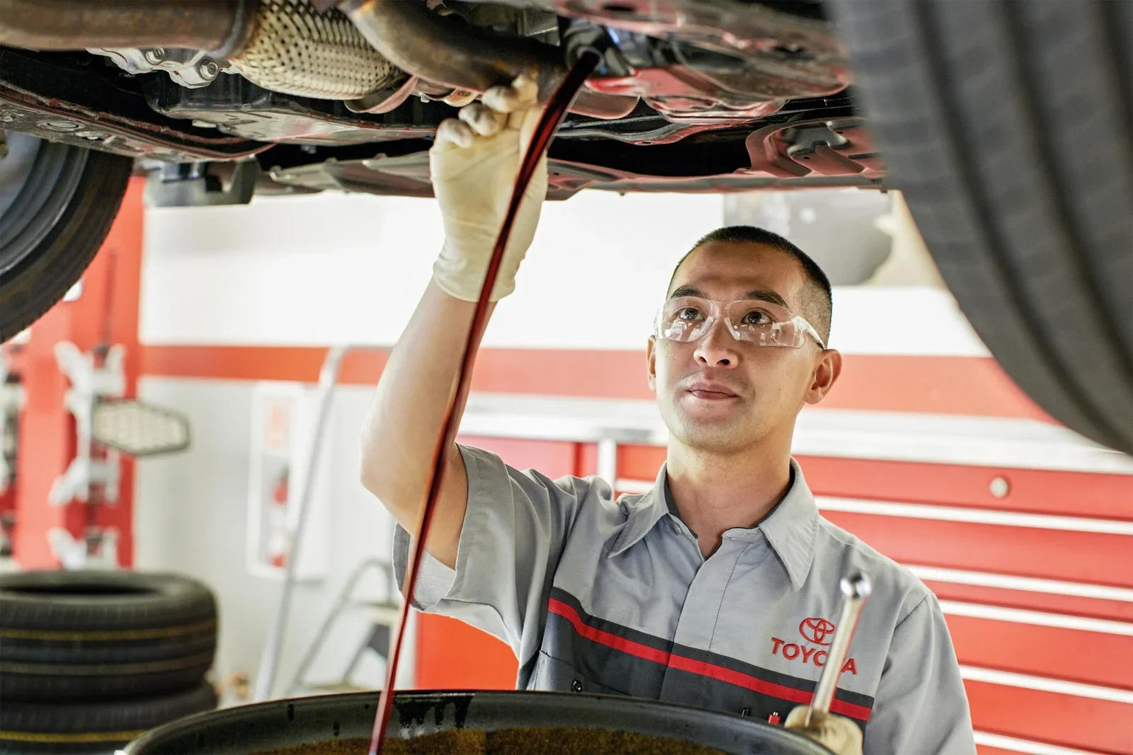 A Toyota technician working underneath a raised car during an oil change